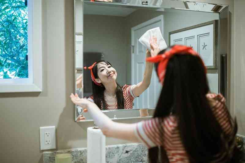 Девушка улыбается и чистит зеркало в ванной
